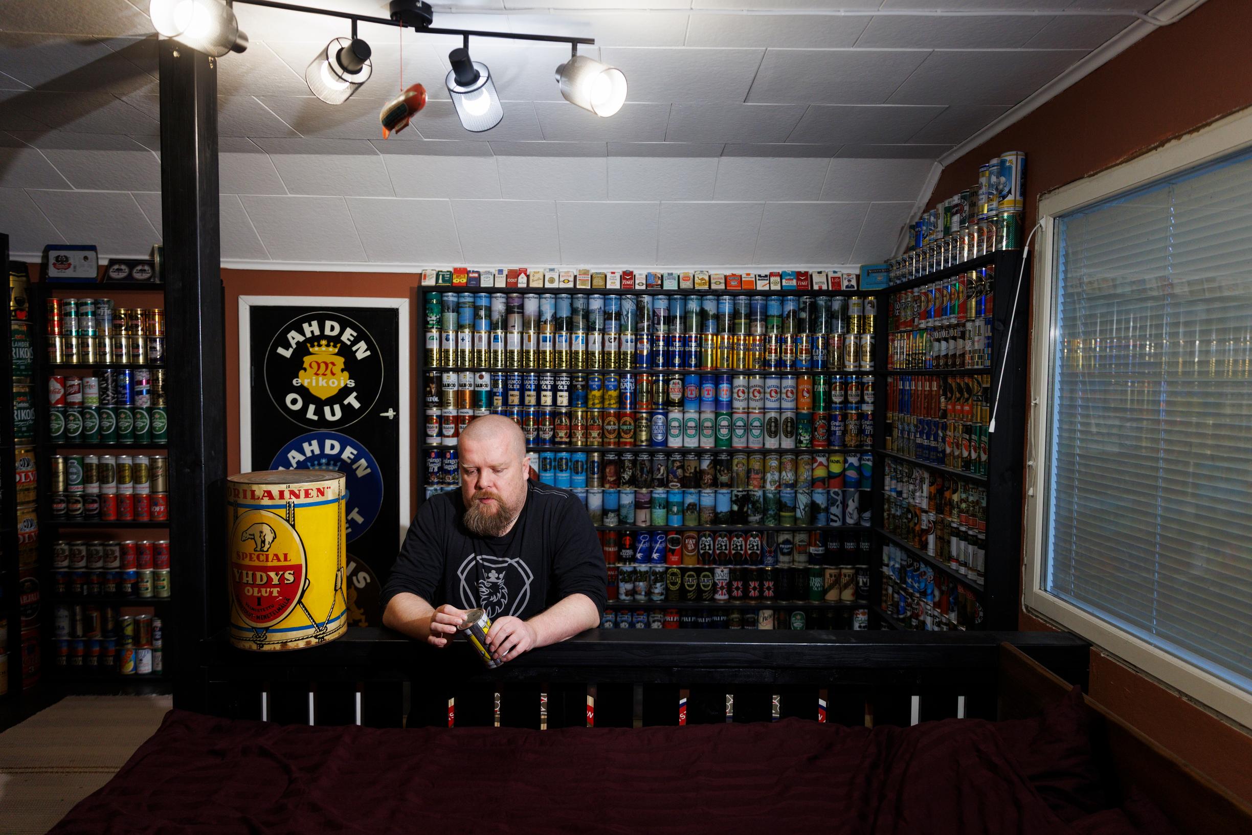 Laajassa kuvassa hyllyrivistö, jossa tölkit siistissä rivissä. Etualla mies nojaamassa baaritiskiin.
