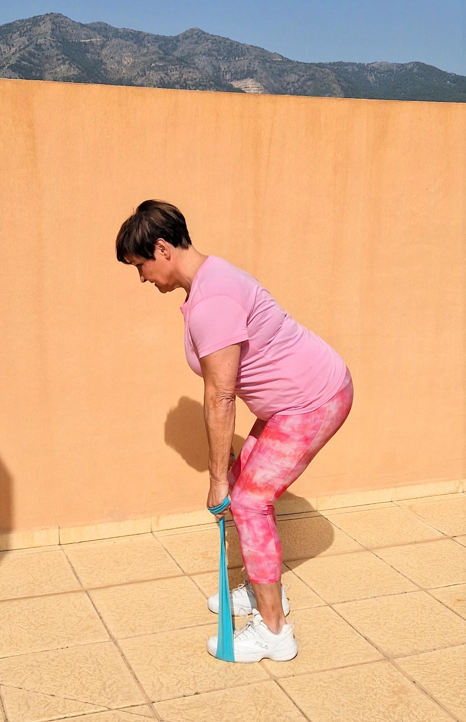 Nainen jumppaamassa: Asetu hartialevyiseen asentoon kuminauha jalkojen alla polvet hieman koukussa. Taivuta lantiosta eteenpäin niska vartalon jatkeena ja vedä napa kohti selkärankaa. Vedä kädet koukkuun lähellä vartaloa ja purista lavat yhteen. Toista liike 10 kertaa ja tee 2–3 sarjaa. Liike vaikuttaa laajasti muun muassa leveään selkälihakseen, lapoihin, syviin vatsalihaksiin, käsien ja jalkojen lihaksiin sekä pakaroihin.