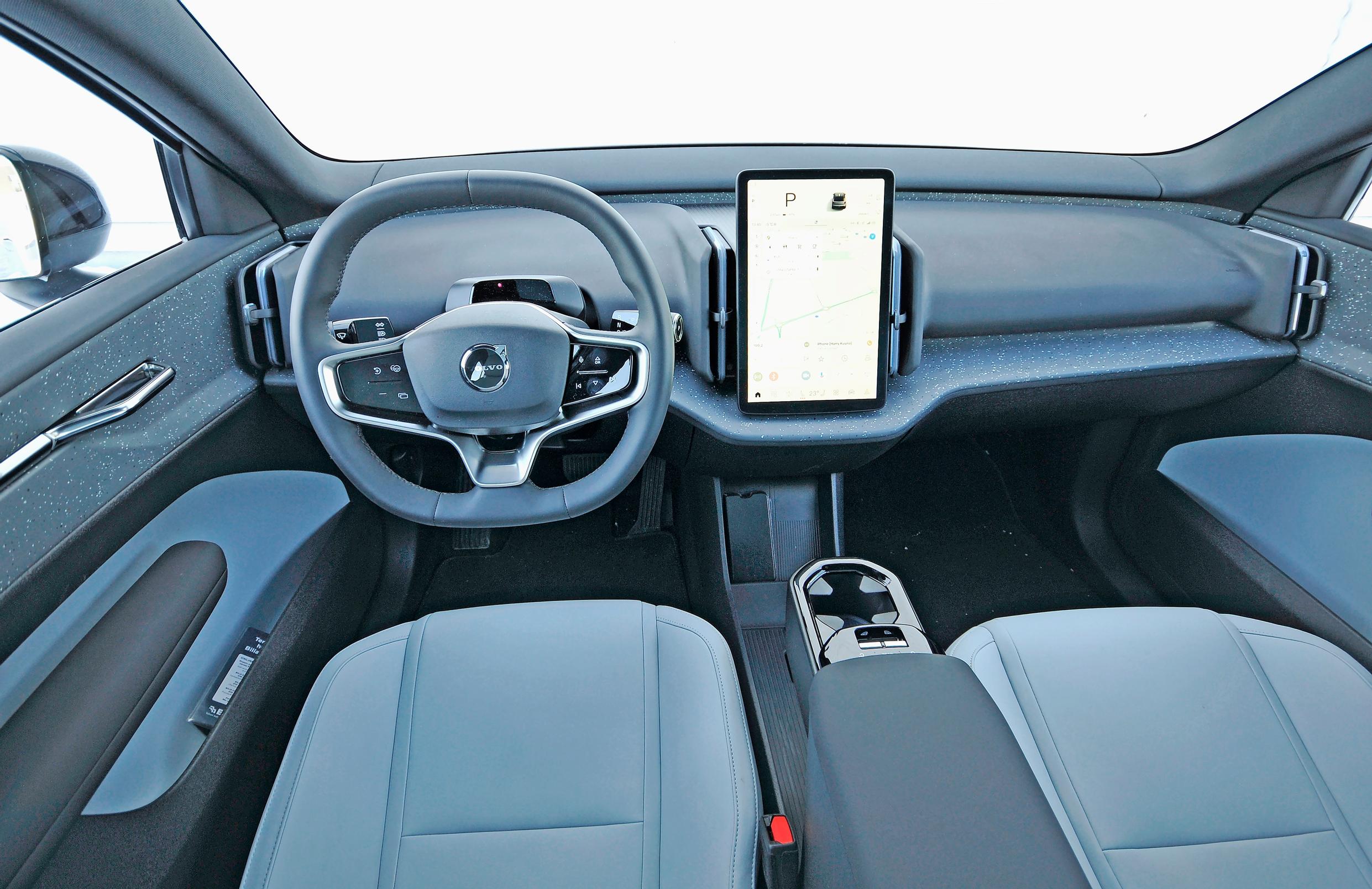Volvo EX30:n napakan tuntuinen ohjauspyörä on litistetty ylä- ja alareunoistaan. Ohjaamossa on vakiona pystysuuntainen 12,3-tuumainen keskinäyttö – eikä sitten ohjauspyörän lisäksi juuri mitään muuta. Edessä on jalkatilaa mukavasti pidemmällekin matkustajalle.