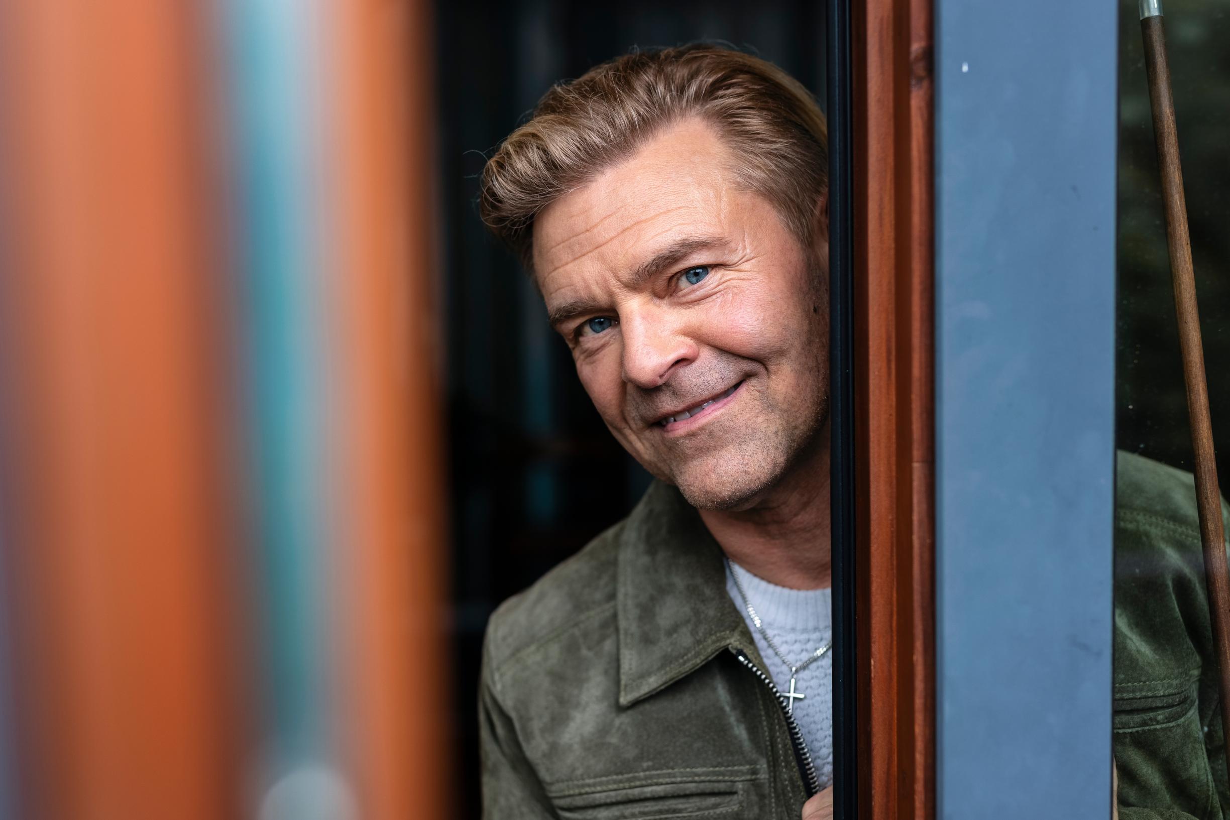 Ressu Redford kurkistaa ovensuusta ja hymyilee.