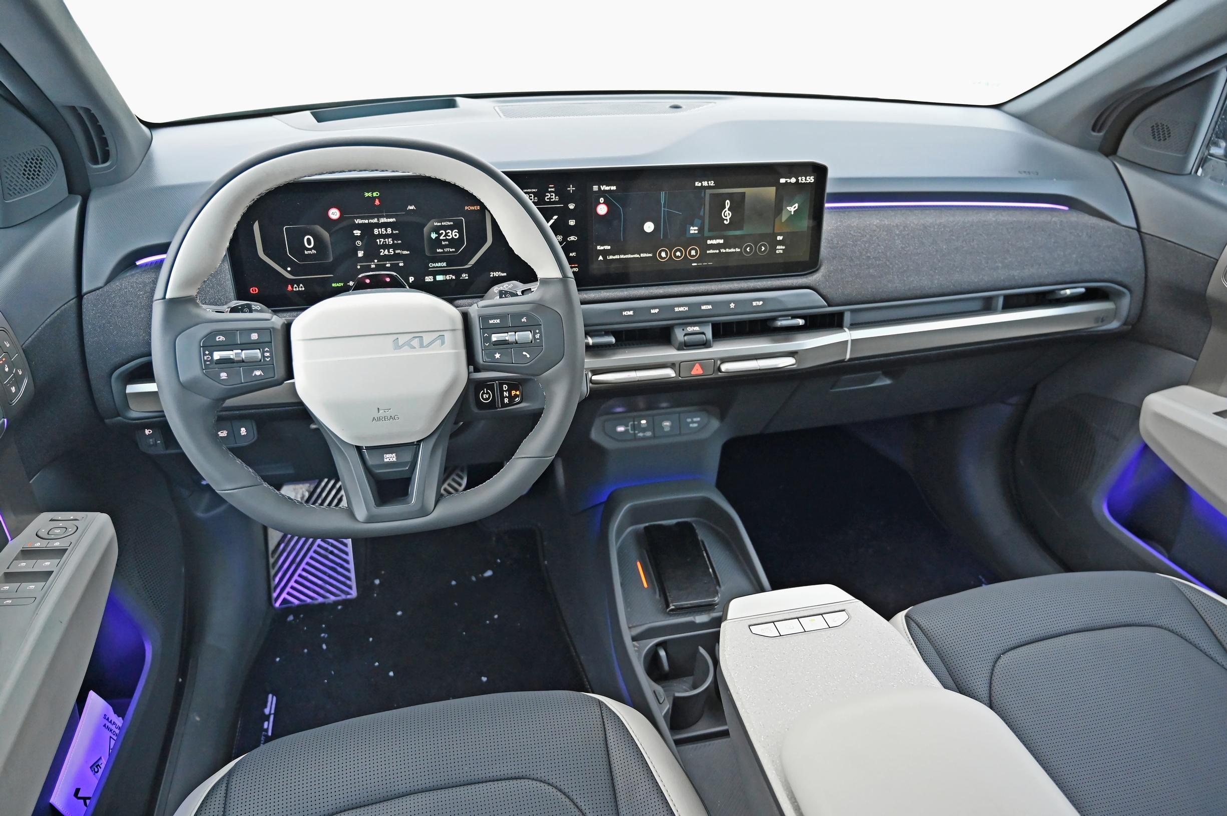 Kia EV 3:n ohjaamo | Vaalein kontrastivärein piristetty paksukehäinen ohjauspyörä on miellyttävä käsitellä. Kookasta keskinäyttöä joutuu kuljettajan paikalta kurottelemaan. Keskikonsoli on matala, ja kännykän latausalusta on sijoitettu helposti tavoitettavaksi.